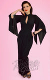 A woman modeling a black floor-length dress with wide draped sleeves and a keyhole cutout at the chest.
