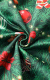 A close-up of a green Christmas-themed fabric with pine tree branches, red ornaments, red poinsettias, and small white star lights, arranged in a swirl. 