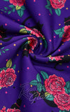 Purple fabric with a bold floral print featuring pink roses, green leaves, black cats and polka dots