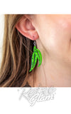 Green leaf-shaped earrings worn by a person with 'Retno Glam' branding.